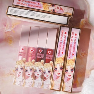 May include: Four clear lip gloss tubes with pink and gold packaging. Each tube features a cartoon image of a girl with blonde hair and a pink heart. The text "KAWAII GIRL LIP GLOSS VINNABELLE" is printed on the tubes.