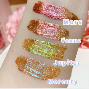May include: Four different shades of glitter eyeshadow, labeled from top to bottom: Mars, Venus, Jupiter, Mercury.