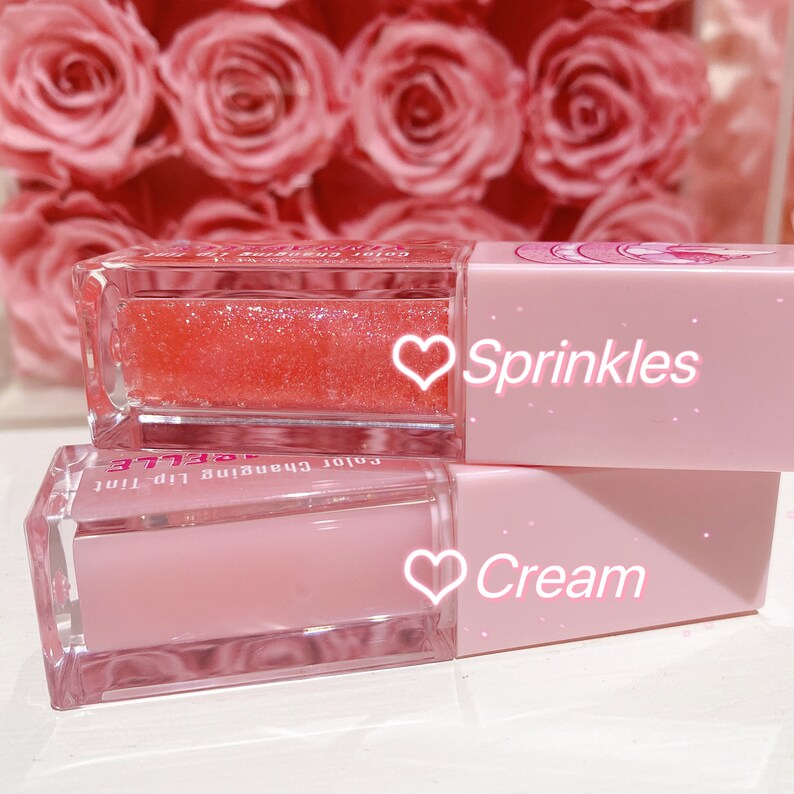 K&ouml;nnte beinhalten: Zwei rosa Lippenpflege-Tuben mit klaren Deckeln. Die obere Tube enth&auml;lt einen rosa-orangenen, farbig wechselnden Lipgloss mit Glitzer. Die untere Tube enth&auml;lt einen klaren rosa Lipgloss. Der Text auf den Tuben lautet "Color Changing Lip Tint" und "Sprinkles" und "Cream".