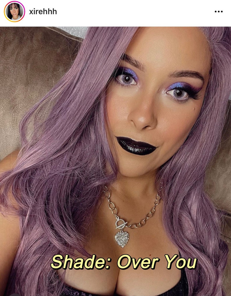 May include: A woman with lavender hair and makeup, including dark lipstick and eye shadow. She wears a silver necklace with a heart pendant. The text "Shade: Over You" is displayed in a yellow font.