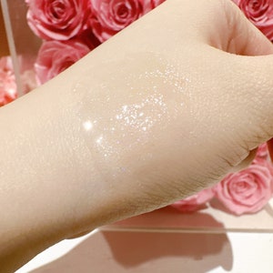 May include: A close-up of a person's hand with a clear, shimmering liquid applied to the skin. The liquid has a subtle sparkle and appears to be a type of lotion or serum.