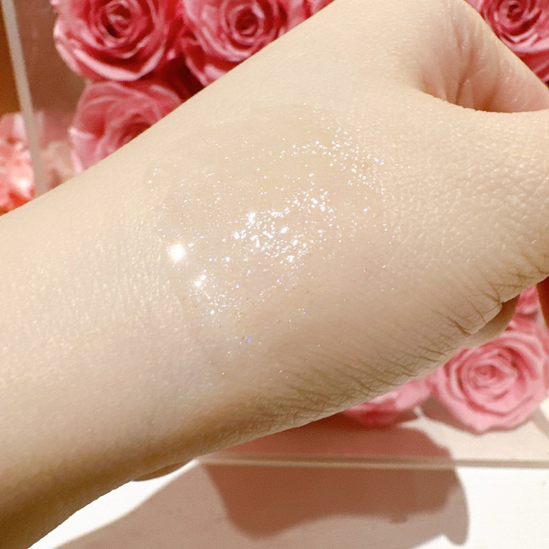 May include: A close-up of a person's hand with a clear, shimmering liquid applied to the skin. The liquid has a subtle sparkle and appears to be a type of lotion or serum.