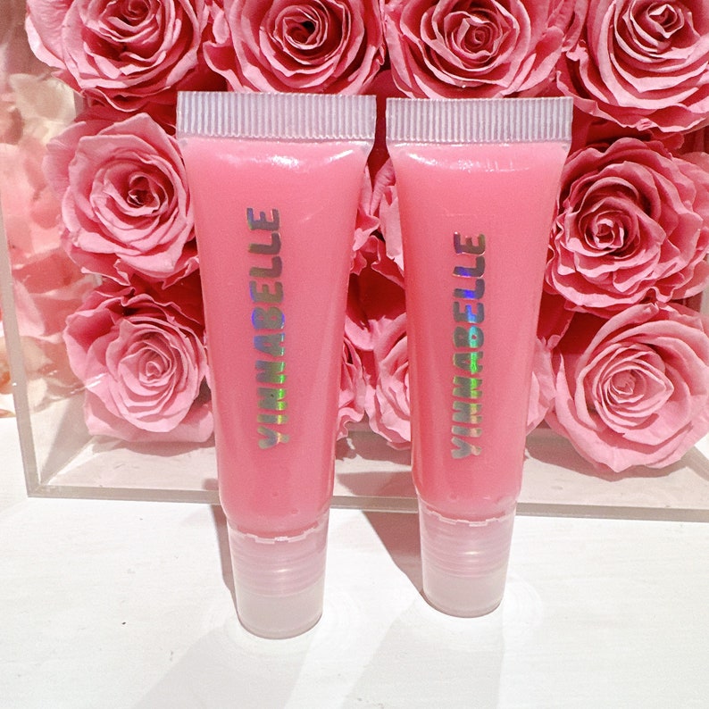 K&ouml;nnte beinhalten: Zwei rosa Lippenpflege-Tuben mit dem Wort "YUMABELLE" in holografischer Schrift auf der Vorderseite.