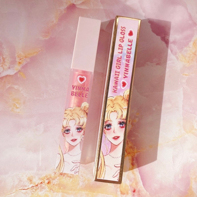 May include: A pink lip gloss tube with a Sailor Moon design and the text "KAWAII GIRL LIP GLOSS VINNABEL  " on the box. The tube has a pink heart with the text "VINNA BELLE" on it.