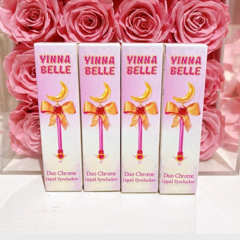 May include: Four bottles of liquid eyeshadow with a pink and white label. The label features a cartoon image of a wand with a crescent moon and a red bow. The text on the label reads "Vinna Belle Duo Chrome Liquid Eyeshadow".