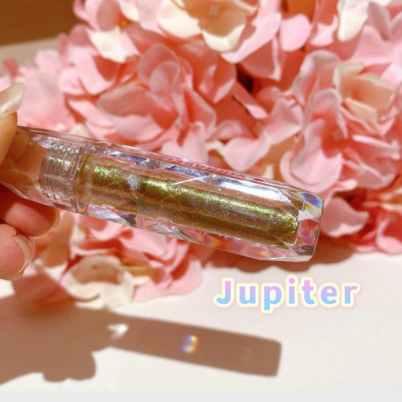 May include: A clear, faceted tube of gold glitter lip gloss with the word "Jupiter" written in rainbow letters below it.
