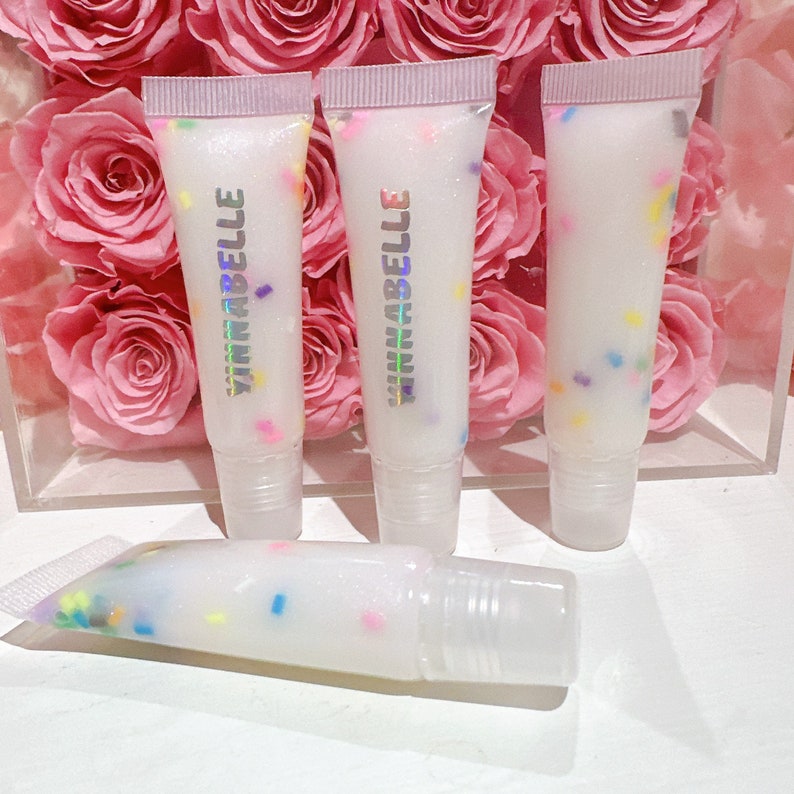 May include: Three clear tubes of lip gloss with a white base and colorful sprinkles. The tubes are labeled "Yinnabelle".