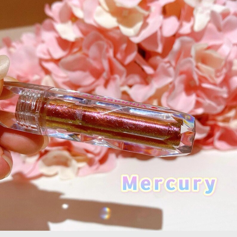 May include: A clear, faceted, tube-shaped container with a metallic, iridescent, red-gold liquid inside. The container is labeled "Mercury".