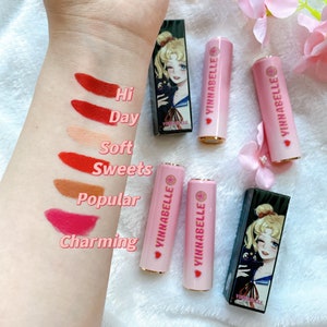 May include: Six pink lipstick tubes with gold accents and a heart design. Each tube has a different color lipstick swatch on the arm. The lipstick swatches are labeled "Hi", "Day", "Soft", "Sweets", "Popular", and "Charming".