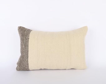 May include: A cream-colored pillow with a brown woven border. The pillow is made of a soft, textured fabric.