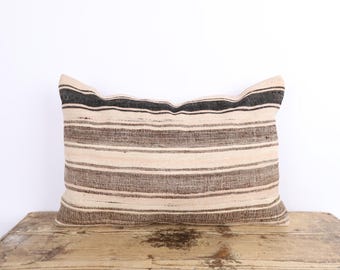 May include: Rectangular pillow with horizontal stripes in shades of beige, brown, and black. The pillow is placed on a wooden surface against a white background. The striped pattern adds a touch of texture and visual interest.