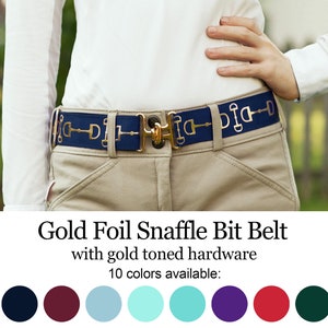May include: Navy blue belt with gold foil snaffle bit design and gold-toned hardware. The belt is worn with khaki pants and a white shirt. The text "Gold Foil Snaffle Bit Belt" is visible.
