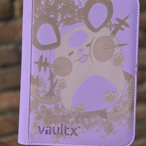 Peut inclure: Un classeur violet clair orné d'un motif graphique marron et violet représentant une créature ronde aux grandes oreilles et à la longue queue. Le texte vaultx est imprimé dans le coin inférieur gauche. La couverture est texturée et arrondie.