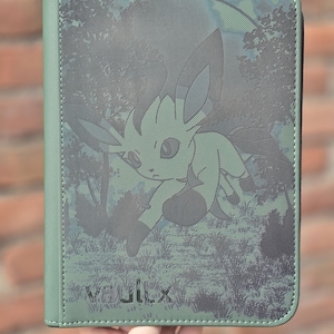 Op de afbeelding: Een rechthoekige groene map met ritssluiting en een donkergroene grafische print van het personage Leafeon in een bosrijke omgeving. De voorkant toont de tekst VaultX in de linkerbenedenhoek, met een gestructureerd oppervlak en gestikte randen.