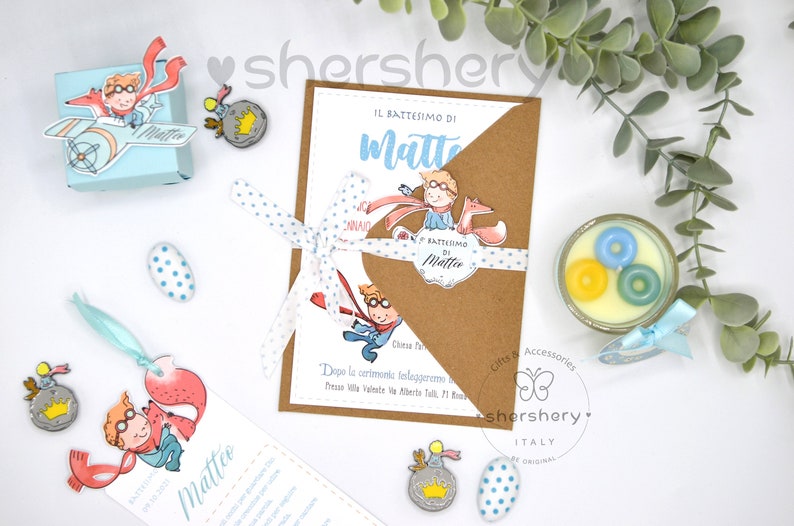 May include: A blue and white invitation for a christening with a Little Prince theme. The invitation features a cartoon illustration of the Little Prince with his fox. The invitation is tied with a blue and white polka dot ribbon. The text on the invitation reads "Il Battesimo di Matteo".