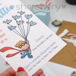 May include: A white invitation card with blue and red illustrations. The card features a boy holding balloons with birds on them. The text on the card reads "IL BATTESIMO DI Matteo DOMENICA 16 GENNAIO ORE 16 Cerimonia Chiesa Parrocchiale di Sant'Isidoro Dopo la cerimonia festeggeremo insieme Presso Villa Valente Via Alberto Tulli, 71 Roma"