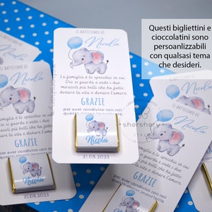 May include: White favor boxes with blue and pink elephant illustrations. The boxes have the text "Il Battesimo di Nicola" and "21.05.2023". The boxes are decorated with blue and white polka dots. The text "Questi bigliettini e cioccolatini sono personalizzabili con qualsasi tema che desideri." is written in black text on a white background.