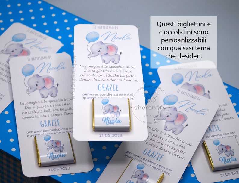 May include: White favor boxes with blue and pink elephant illustrations. The boxes have the text "Il Battesimo di Nicola" and "21.05.2023". The boxes are decorated with blue and white polka dots. The text "Questi bigliettini e cioccolatini sono personalizzabili con qualsasi tema che desideri." is written in black text on a white background.