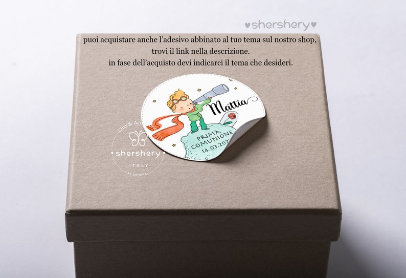 May include: A beige gift box with a round sticker featuring a cartoon illustration of a boy with a telescope, a red scarf, and a small rose. The sticker says "Mattia" and "Prima Comunione 14.03.2022".
