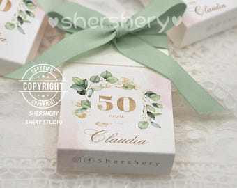 May include: A white gift box with a green ribbon and bow. The box has a floral design with gold accents and the text "50 anni Claudia" and "@f Shershery".