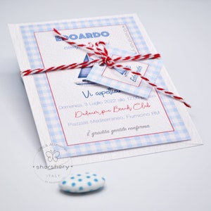 May include: A white invitation with blue and white checkered pattern. The invitation is tied with a red and white twine. The invitation text reads "Vi aspettiamo Domenica, 3 Luglio 2022 alle 17:00 Dadaumpa Beach Club Piazzale Mediterraneo, Fiumicino RM &Egrave; gradita gentile conferma".