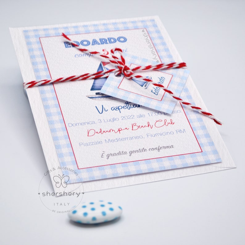 May include: A white invitation with blue and white checkered pattern. The invitation is tied with a red and white twine. The invitation text reads "Vi aspettiamo Domenica, 3 Luglio 2022 alle 17:00 Dadaumpa Beach Club Piazzale Mediterraneo, Fiumicino RM &Egrave; gradita gentile conferma".