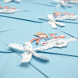 May include: A stack of light blue envelopes with white polka dot ribbon and a small illustration of a boy with a fox. The envelope has the text "Il Battesimo di  [Name]" printed on it.