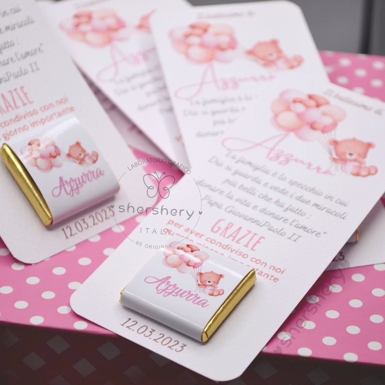 May include: A white chocolate bar with a pink and gold design. The bar features a cartoon bear holding pink balloons and the text "Azzurra" and "12.03.2023".