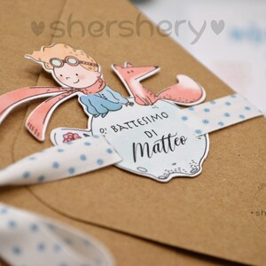 May include: A brown paper envelope with a blue and white polka dot ribbon tied around it. The envelope has a sticker on it with a cartoon image of a boy with a fox. The sticker says "O' Battesimo di Matteo".