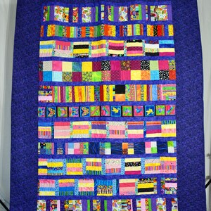 Peut inclure: Une courtepointe colorée avec un motif de patchwork présentant diverses formes géométriques et motifs. La courtepointe est composée de différents tissus dans des tons de rose, jaune, vert, bleu et violet. La courtepointe est affichée sur un fond bleu foncé.