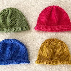 May include: Four knitted hats in different colors: green, pink, blue, and yellow. The hats are all the same style, with a simple, rounded crown and a folded brim.