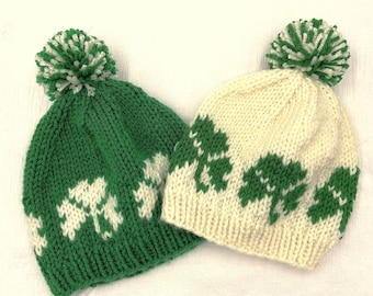 May include: Two knitted hats with pom-poms. One hat is green with white shamrock designs and the other is white with green shamrock designs.