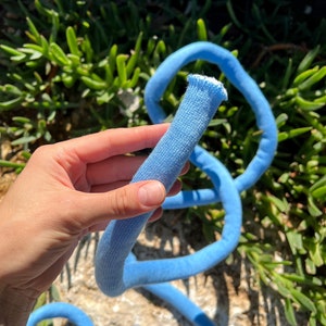 May include: A light blue cotton rope, coiled and held in a hand. The rope is soft and flexible, perfect for crafting or decoration.