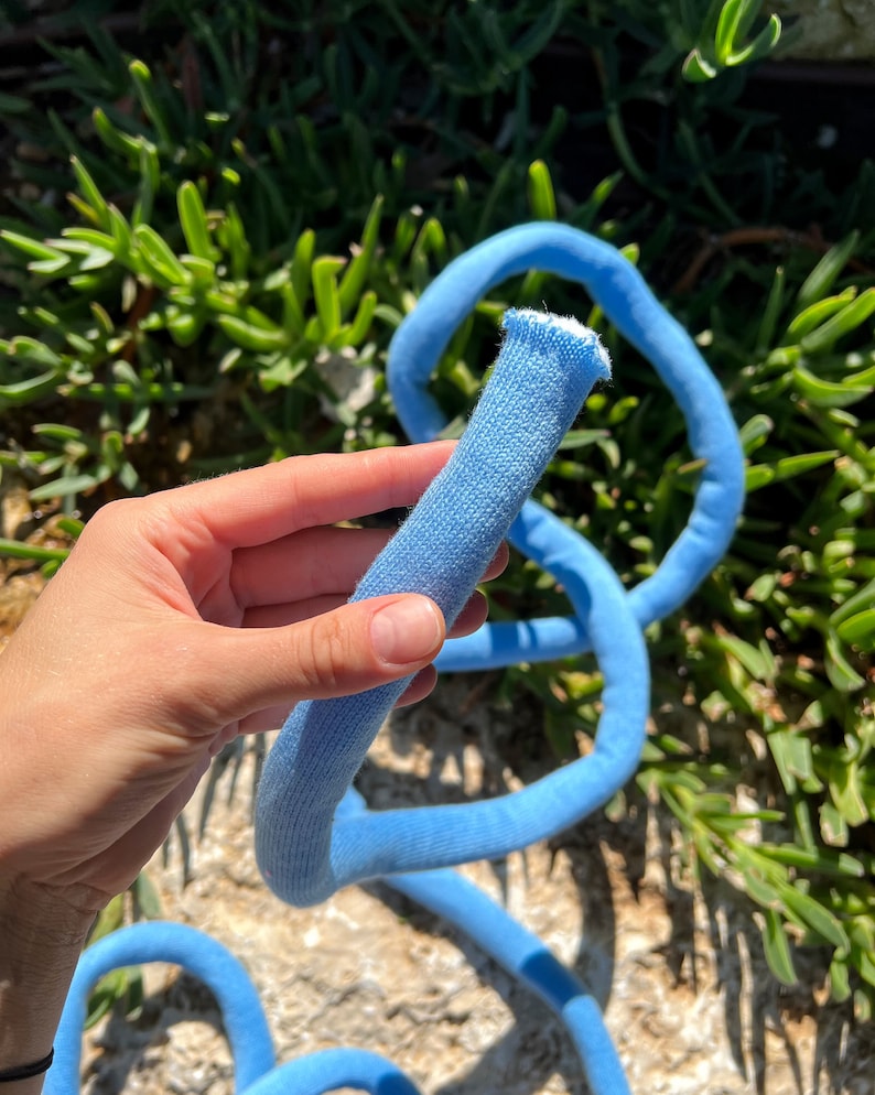 May include: A light blue cotton rope, coiled and held in a hand. The rope is soft and flexible, perfect for crafting or decoration.