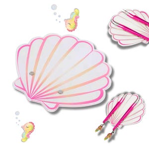 Op de afbeelding: Een roze schelpvormig dienblad met twee magnetische sluitingen. Het dienblad is versierd met een wit en roze ombre-ontwerp. Twee roze pincetten met zeepaardjescharms worden op het dienblad getoond.