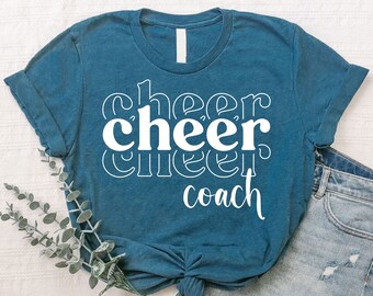 May include: A teal blue t-shirt with white text that reads "cheer cheer cheer coach".