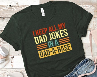 May include: A dark green t-shirt with a vintage-style graphic that reads "I keep all my dad jokes in a dad-a-base".