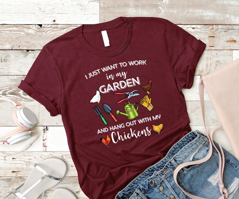 May include: Burgundy t-shirt with the text "I just want to work in my garden and hang out with my chickens". The shirt features a variety of gardening tools and chickens.