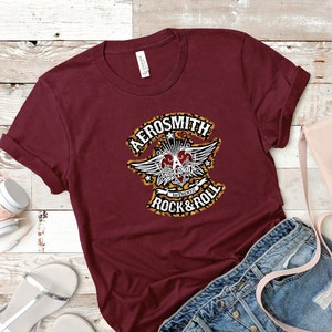 May include: A maroon t-shirt with a graphic print of a heart with wings and the text "Aerosmith Authentic Rock & Roll".