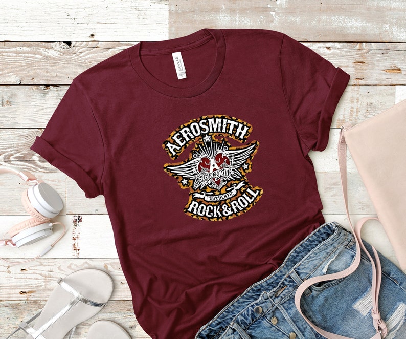 May include: A maroon t-shirt with a graphic print of a heart with wings and the text "Aerosmith Authentic Rock & Roll".
