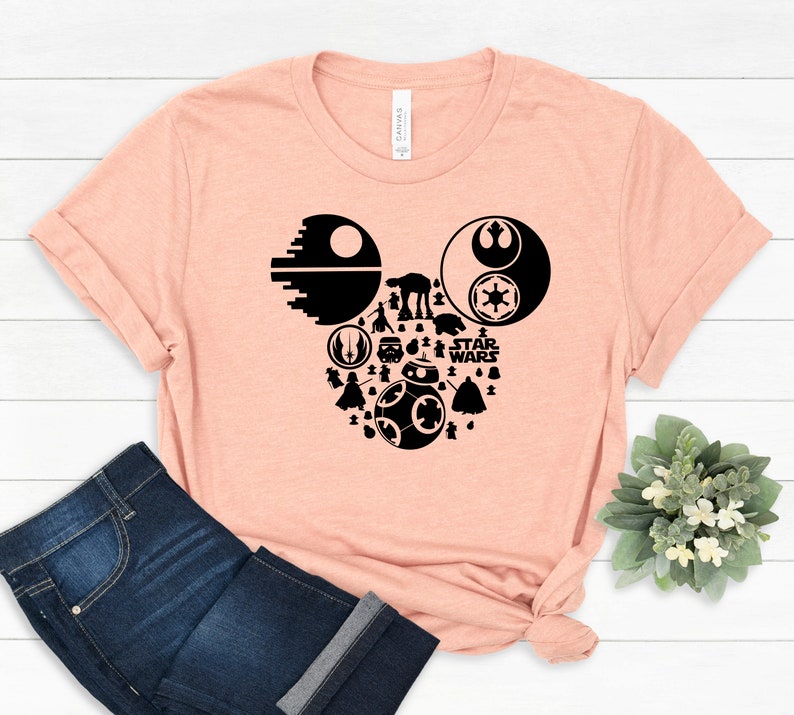 May include: A peach-colored t-shirt with a black silhouette of Mickey Mouse's head made up of Star Wars characters and symbols, including Darth Vader, R2-D2, Yoda, and the Death Star. The text "STAR WARS" is also included in the design.