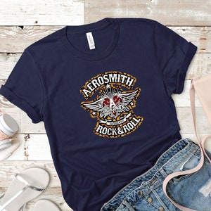 May include: A navy blue t-shirt with a graphic print of the Aerosmith logo. The logo features a heart with wings and the text "Aerosmith" and "Authentic Rock & Roll".