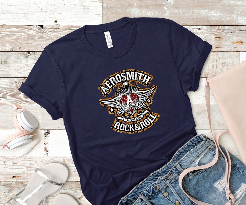 May include: A navy blue t-shirt with a graphic print of the Aerosmith logo. The logo features a heart with wings and the text "Aerosmith" and "Authentic Rock & Roll".