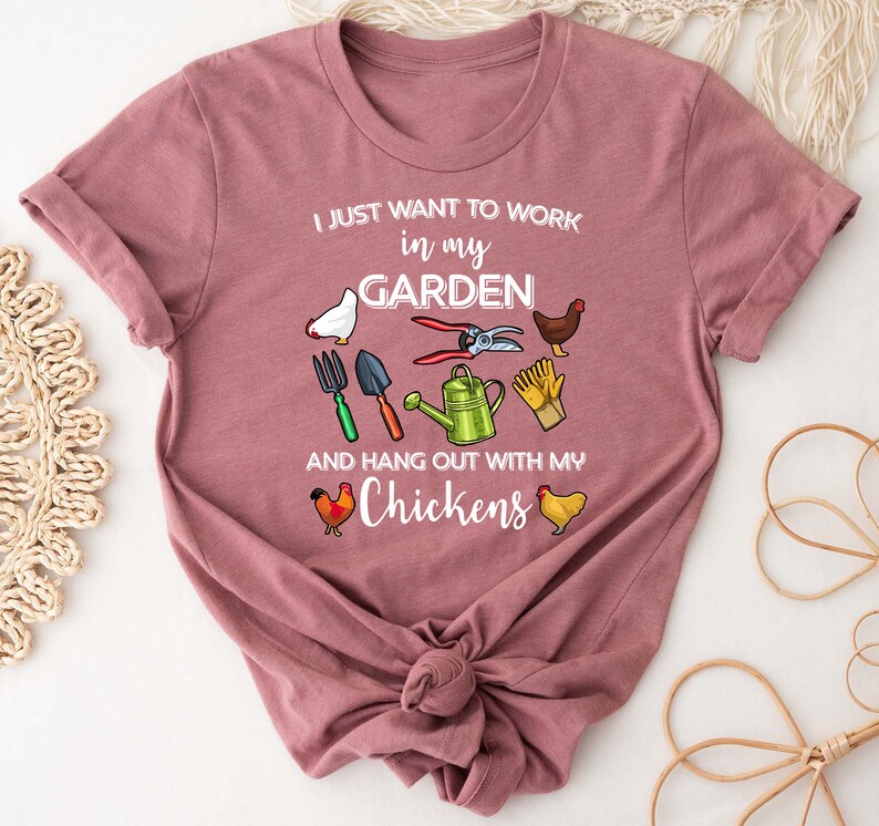 May include: A pink t-shirt with the text "I just want to work in my garden and hang out with my chickens". The shirt features a variety of gardening tools and chickens.