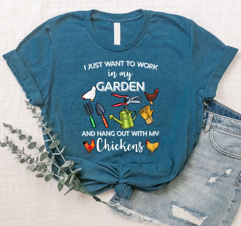 May include: A teal blue t-shirt with the text "I just want to work in my garden and hang out with my chickens". The shirt features a variety of gardening tools and chickens.