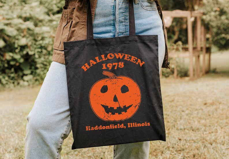 May include: A black tote bag with a white graphic of a pumpkin with a scary face. The text "HALLOWEEN 1978 Haddonfield, Illinois" is printed on the bag.