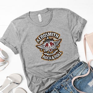 May include: Gray t-shirt with a black and white graphic of the Aerosmith logo. The logo features a heart with wings and the text "Authentic Rock & Roll".