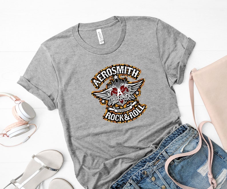 May include: Gray t-shirt with a black and white graphic of the Aerosmith logo. The logo features a heart with wings and the text "Authentic Rock & Roll".