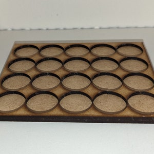 May include: A rectangular tan wooden tray featuring a grid of twenty circular cutouts arranged in four rows of five. The edges of the circular openings are finished in a dark brown colour, contrasting with the light tan surface of the wood board.