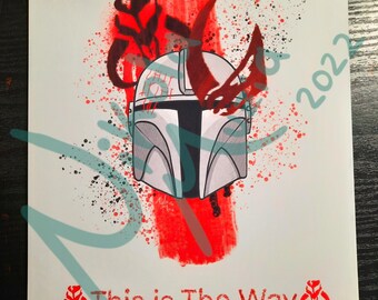 May include: A white and gray Mandalorian helmet with red and black splatters of paint. The helmet is surrounded by a red brush stroke and the text "This is The Way" is below the helmet.